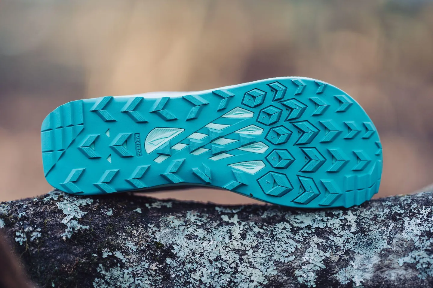 The Altra Lone Peak 7 sits sideways on a rock, exposing the outsole.
