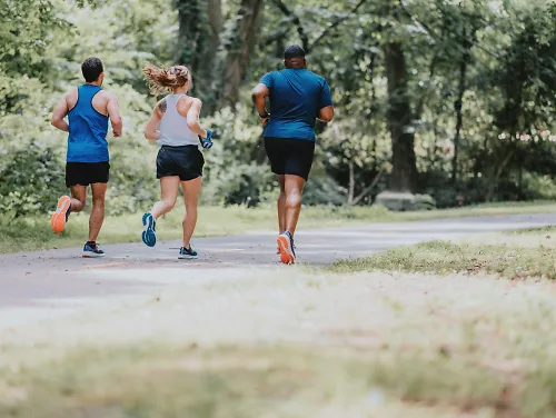 Three runners run on a paved greenway trail together.