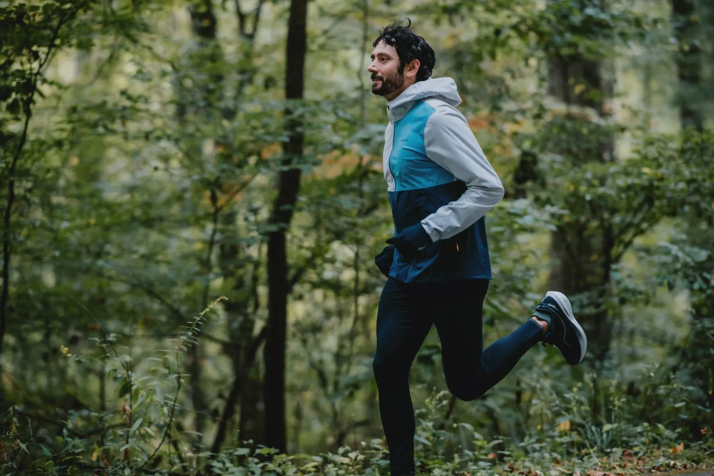 A man runs through the woods, smiling.