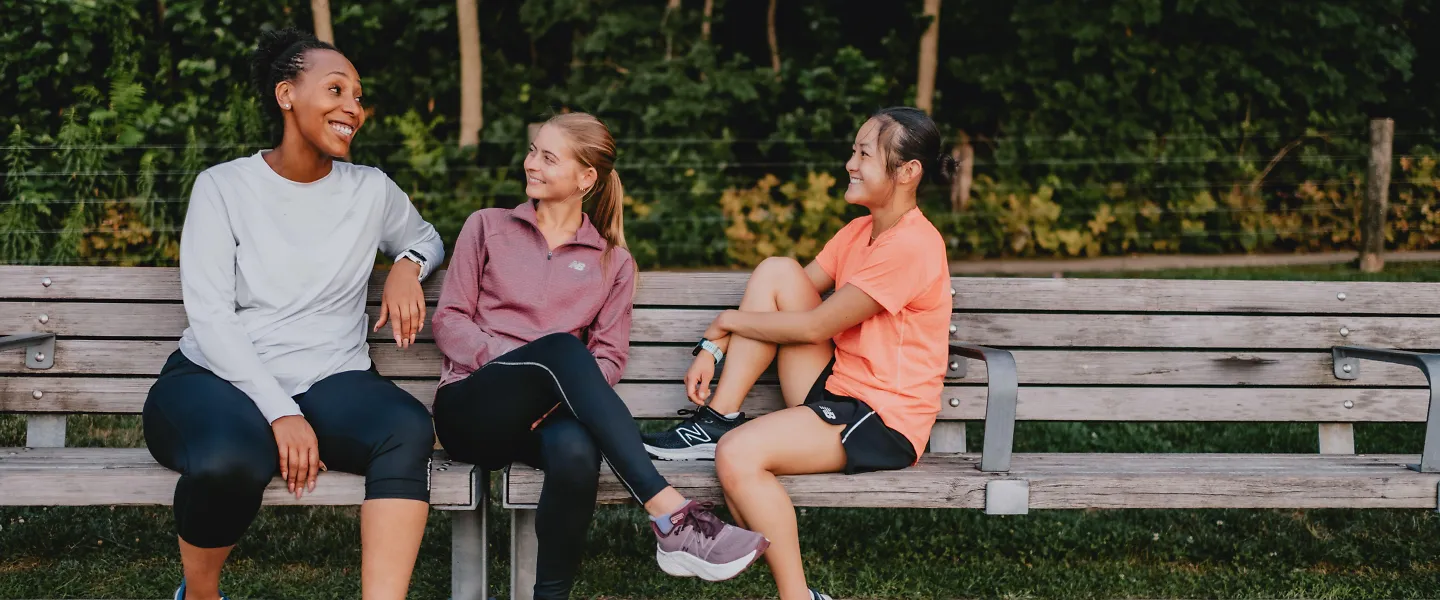 Three woman talk and laugh on a park bench.