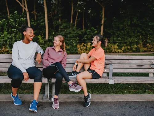 Three woman talk and laugh on a park bench.