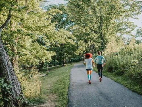 Two runners run along a greenway path.