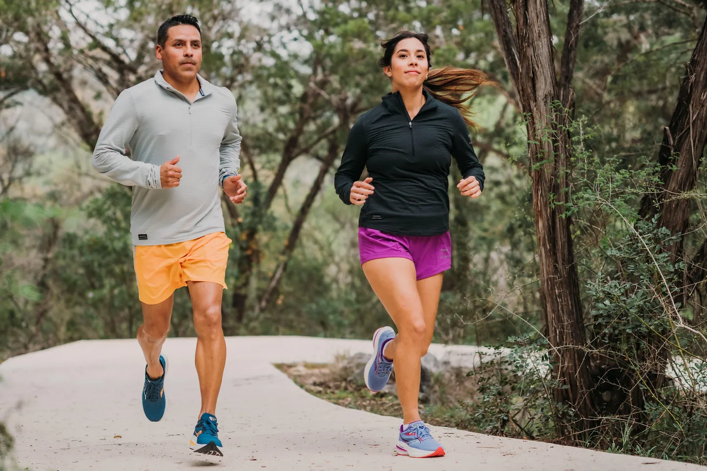 A man and woman run alongside a tree-lined path.