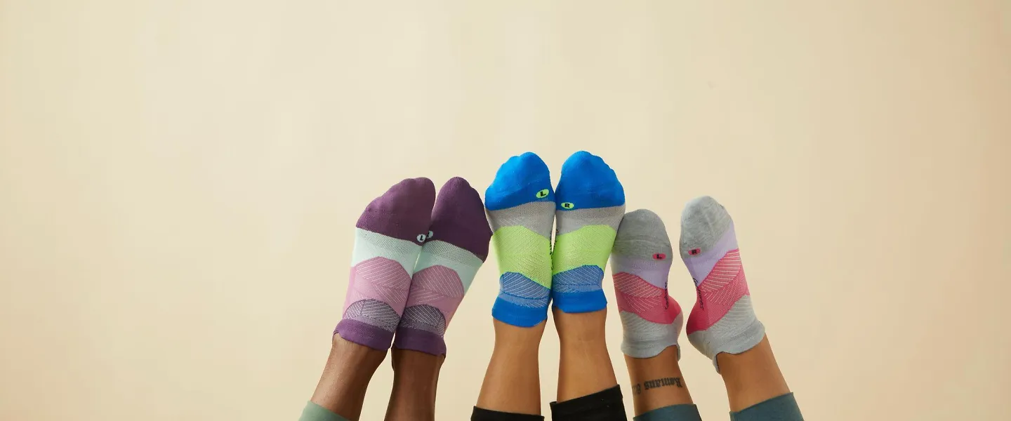 Three runners wearing Feetures socks with their feet up in the air.
