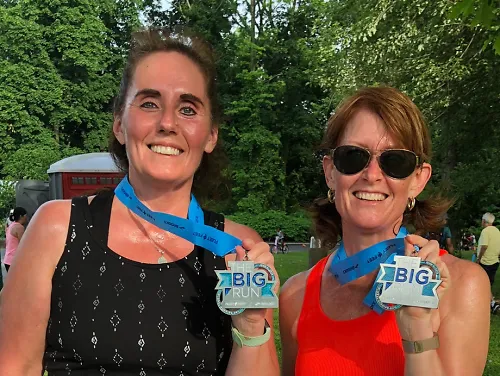 Two smiling women hold out their race medals