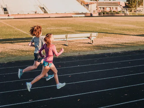 Two girls run around an outdoor track.