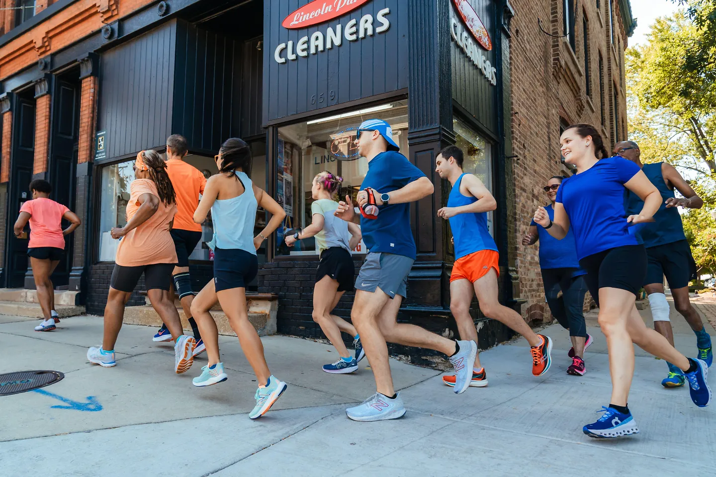 A group of runners run past a dry cleaning shop. 