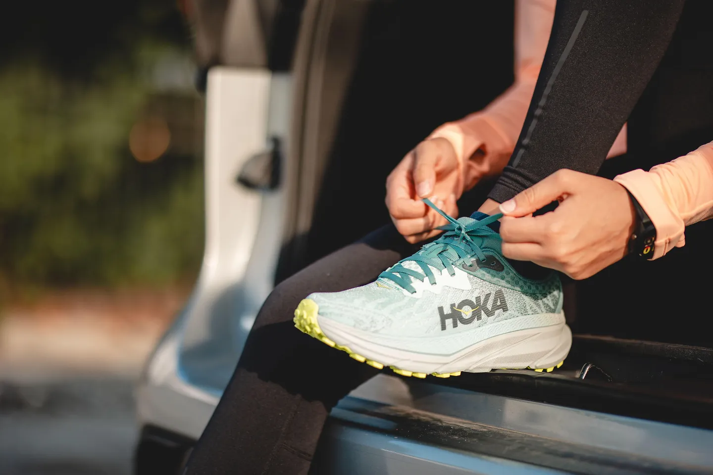 A woman laces up a pair of HOKA running shoes.