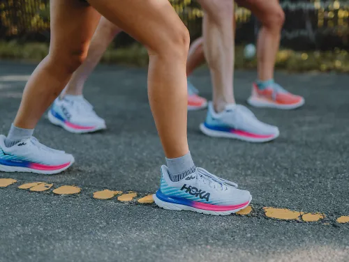 Three runners stand on a paved pathway in the HOKA Mach 5.
