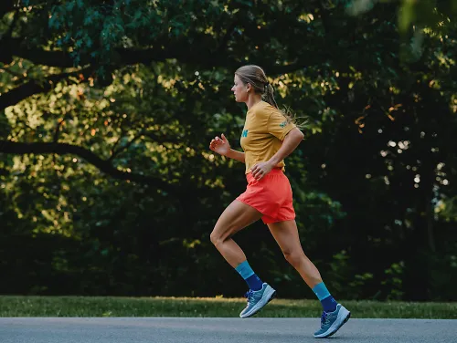 A woman runs down a sun soaked road. 