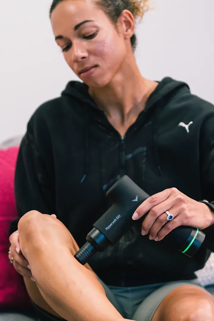 A woman uses a massage gun on her calf