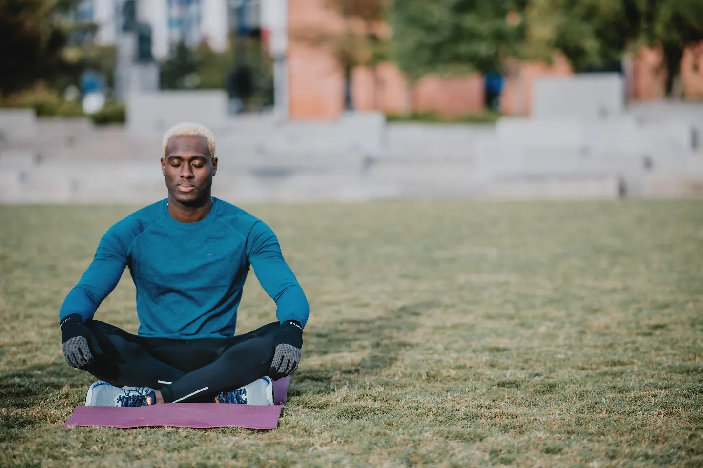A man meditates on a yoga mat inside a park.