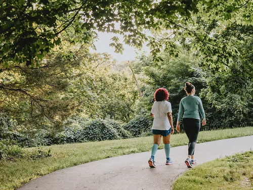 Two women walk on a shaded pathway.