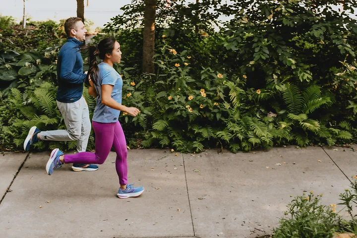A man and woman run together on a sidewalk.