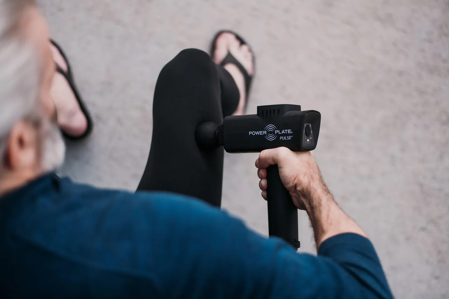 A man holds a massage gun up to his quad muscle.