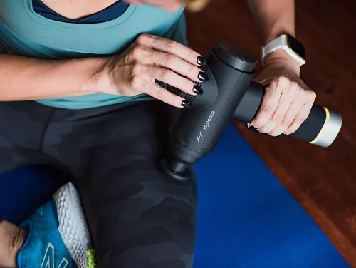 A woman uses a massage gun on her quads. 