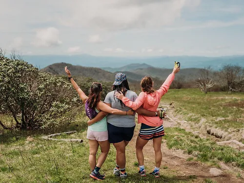 Three runners stand on top of a mountain.