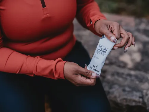 A woman holds up a Maurten Caf gel. 