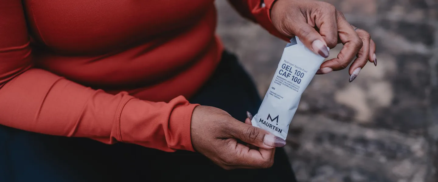 A woman holds up a Maurten Caf gel. 