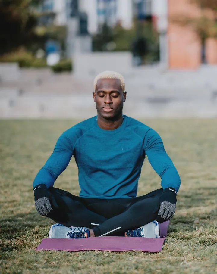 A man sits outside with his legs crossed on a yoga mat. 