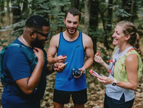 three runners pause on their trail run to talk, drink water and eat snacks