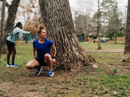 Woman squatting behind a tree while another woman looks out