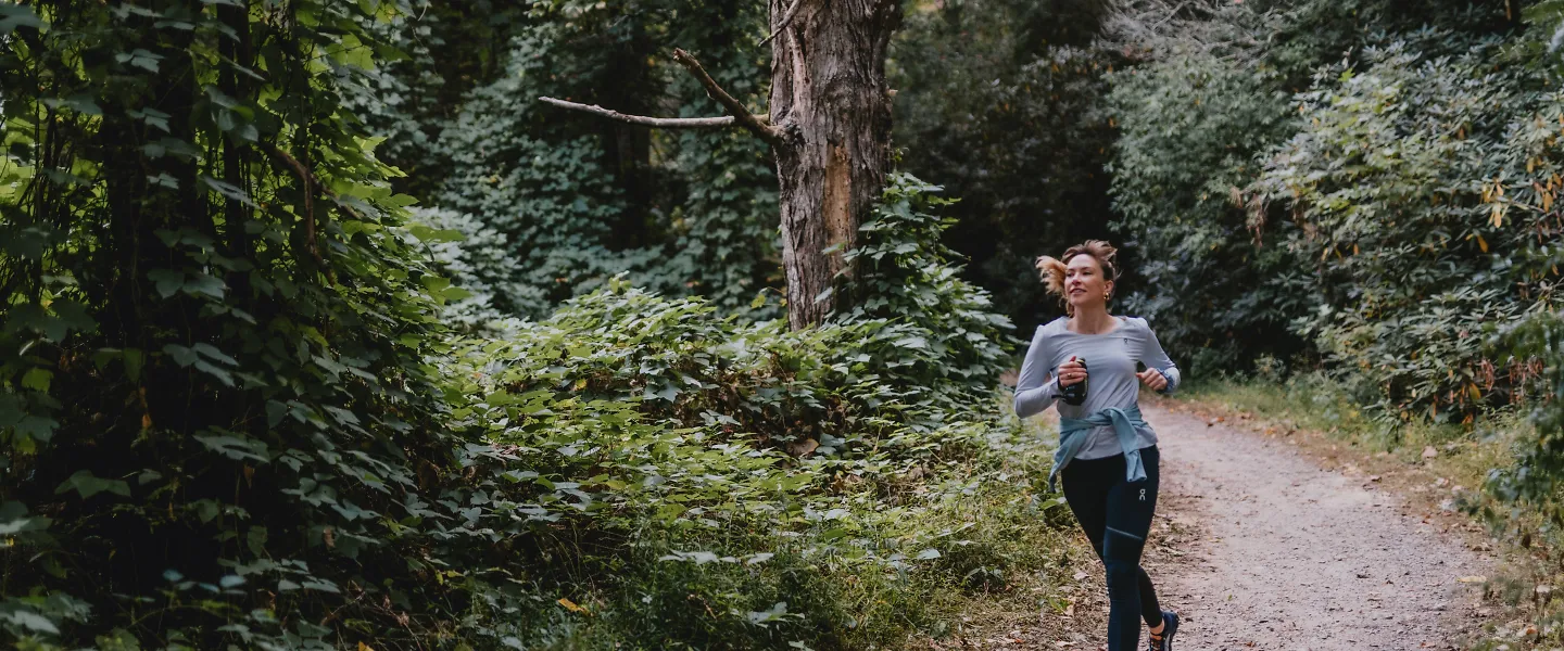 A woman runs down a wooded path.