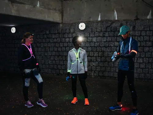 Three runners stand in a dark tunnel wearing visibility gear