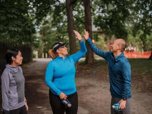 Two runners high-five while another runner looks on.