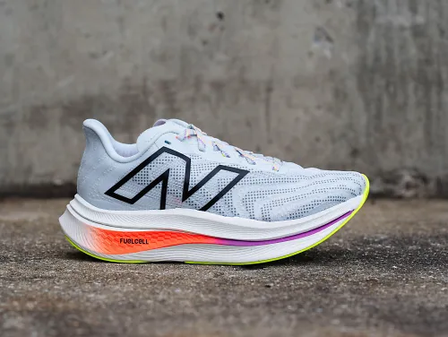 The New Balance FuelCell SuperComp Trainer v2 sits sideways on a slab of concrete. 