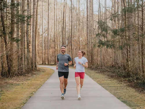 A man and woman run together down a greenway path.