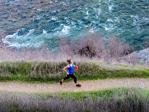 A woman runs on a trail next to a river