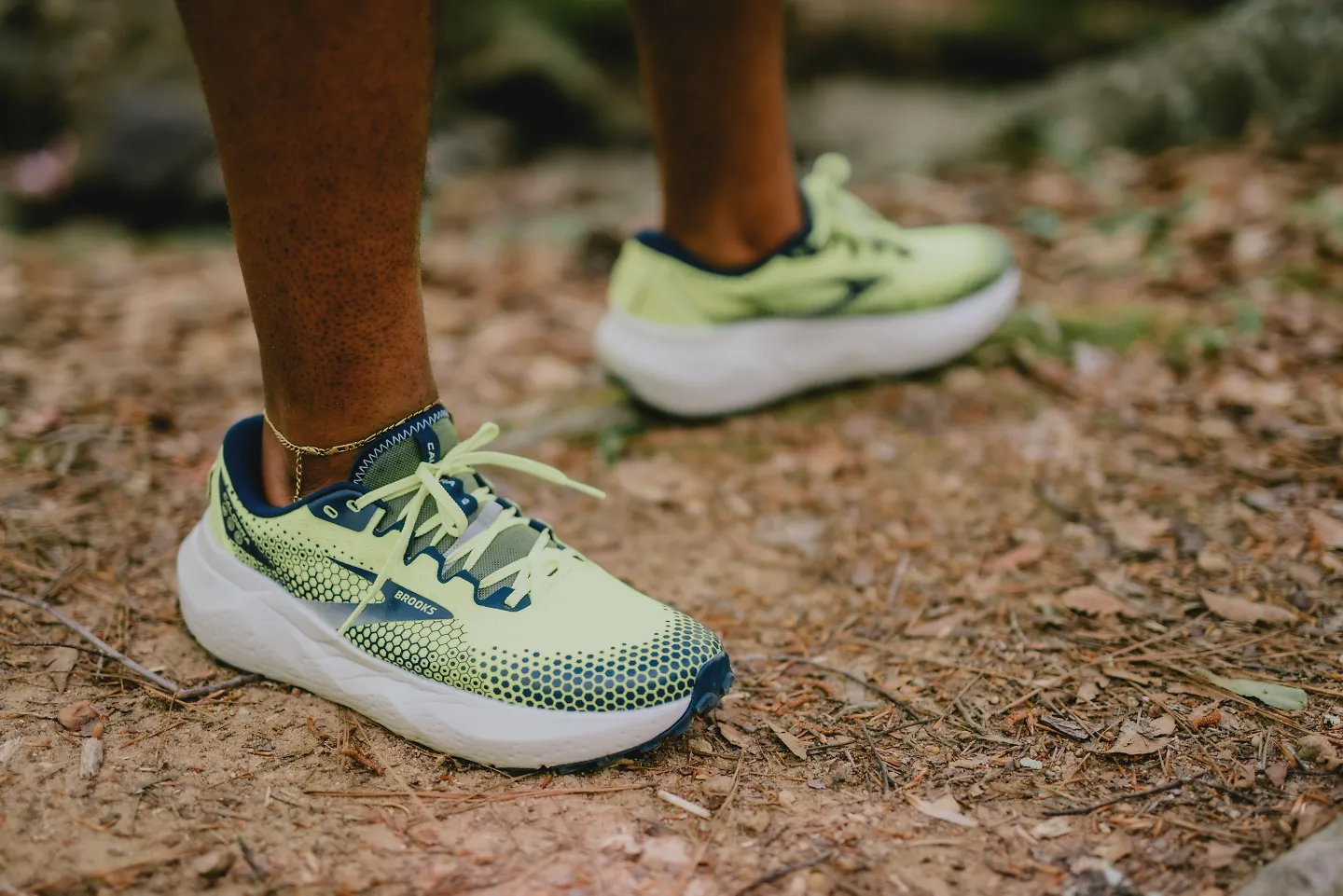 A man wearing the Brooks Caldera 6 stands on a packed trail.