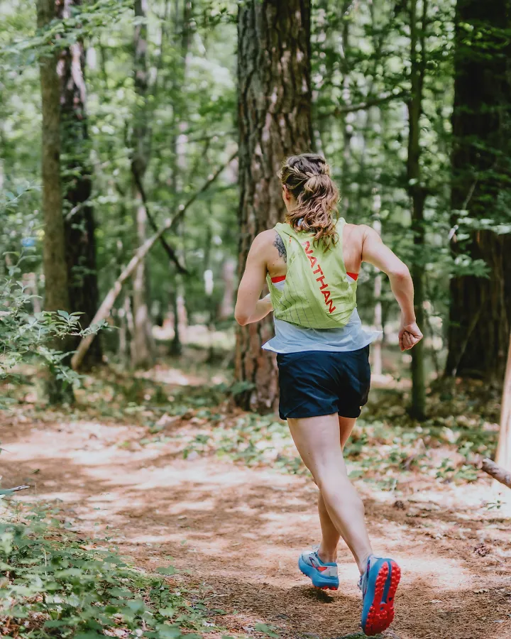 A woman runs through the woods wearing trail running shoes.