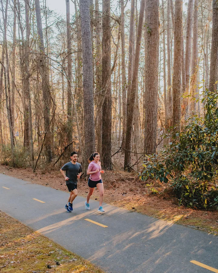 Two runners run through a tree-lined greenway.