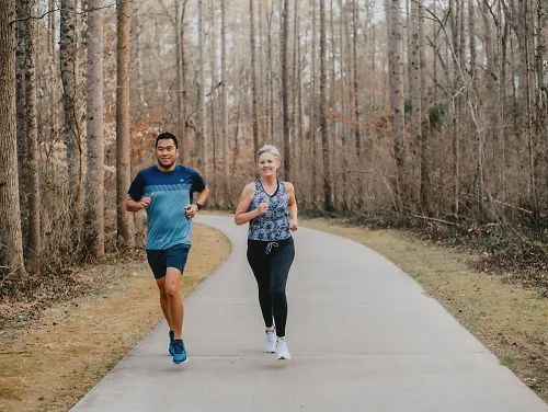 A man and woman run down a greenway path.