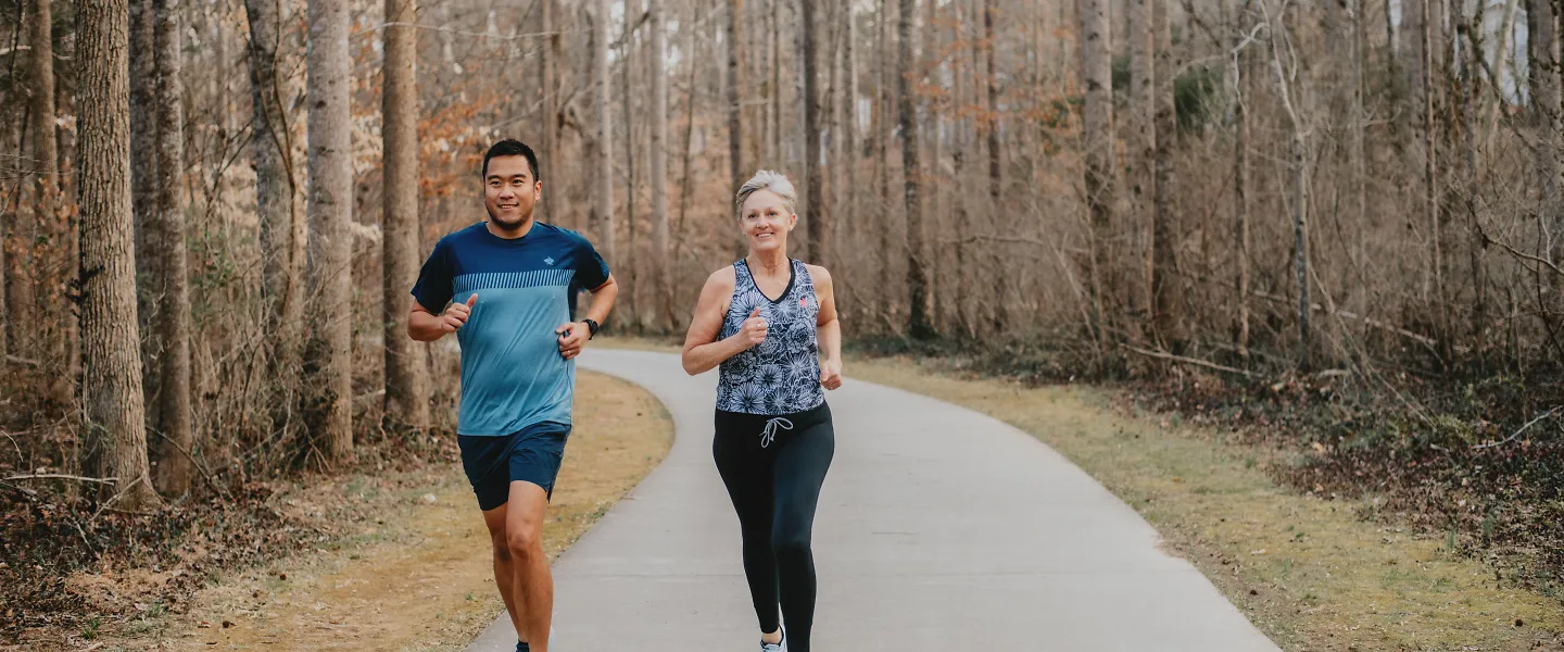 A man and woman run down a greenway path.