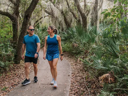 A man and woman walk through a shaded preserve together.