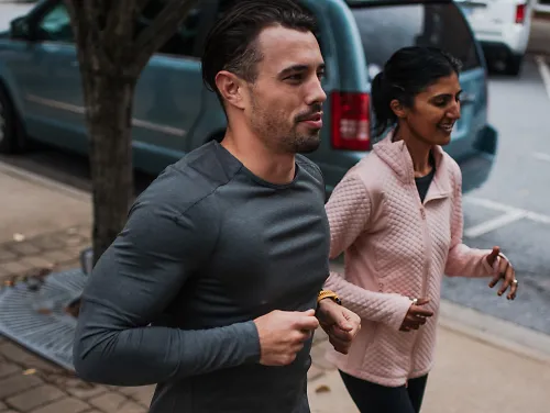 Two runners run on a sidewalk together