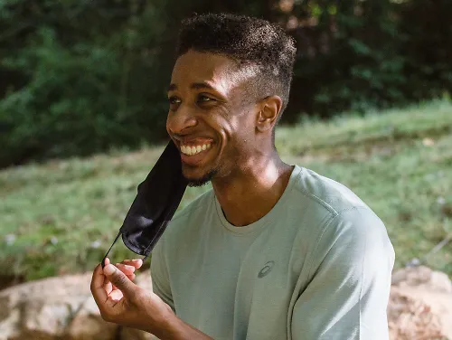 A man smiles as he pulls off his facemask