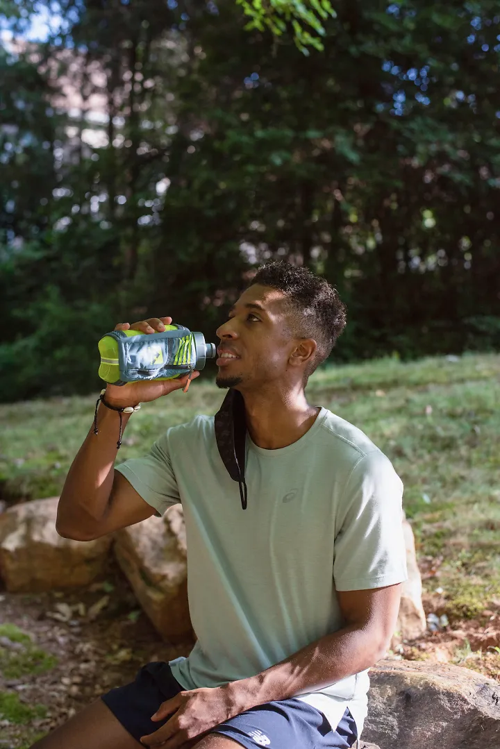 A runner removes his mask to drink from a handheld bottle