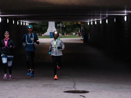 three runners run together in the dark through a tunnel wearing lights and reflective gear
