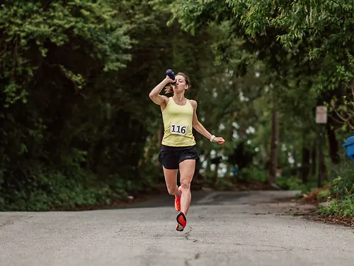 A young woman races down a street and drinks from a waterbottle