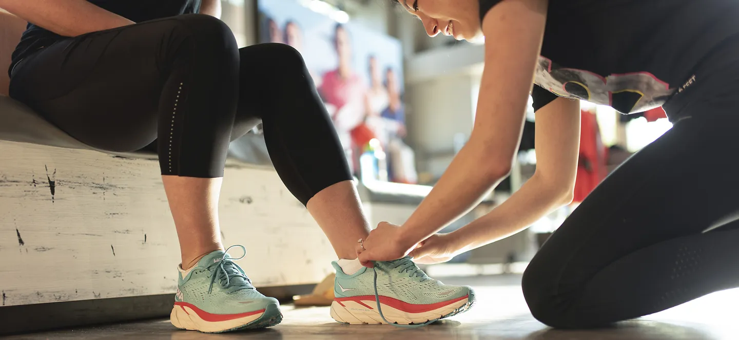 A woman bends to tie a shoe on a customer's foot at Fleet Feet