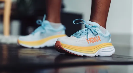 A pair of blue and yellow HOKA Bondi 8 shoes standing on a dark floor