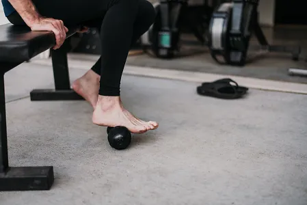 A man's foot is shown as he rolls a massage device underneath it. 