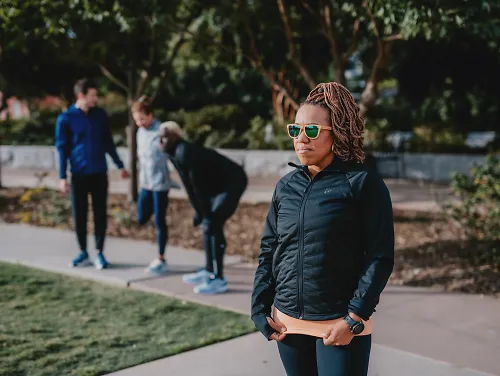 Woman wearing sunglasses standing in front of running group.