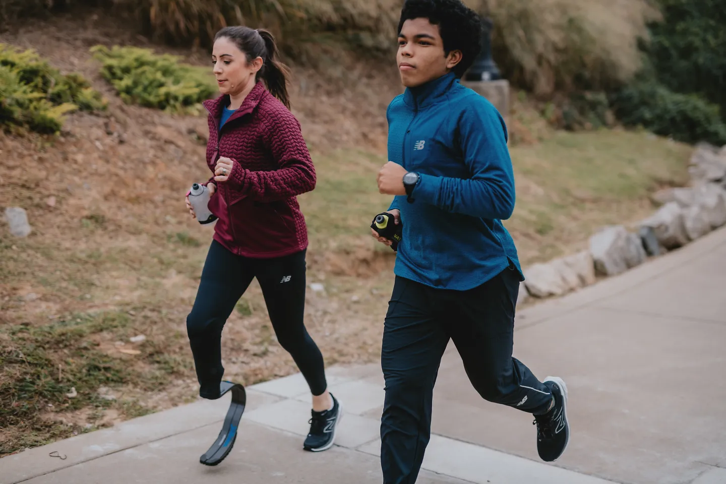 Two runners run with hydration bottles.