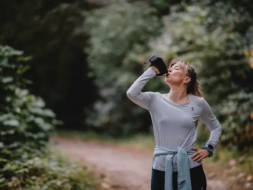 A woman sips from a water bottle during her run.