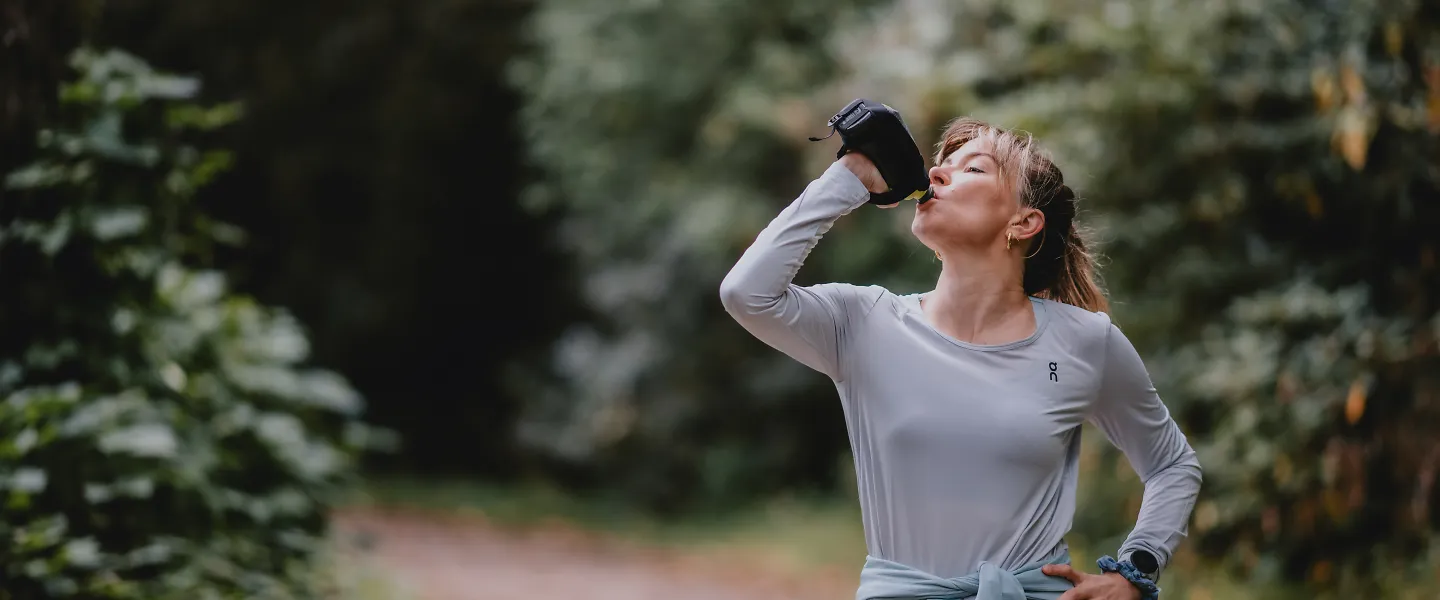 A woman sips from a water bottle during her run.